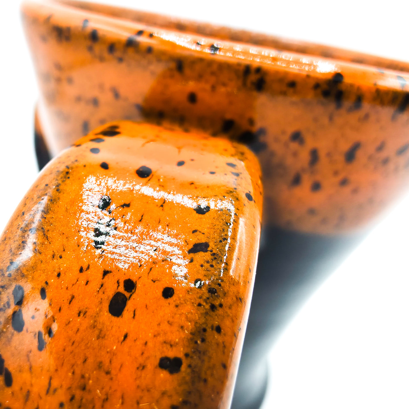 Close-up of an orange ceramic bowl with black speckles on a white background