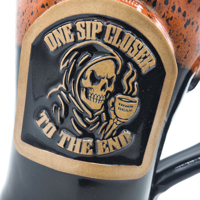 Mug with a decorative emblem featuring a skull holding a coffee cup and text 'One Sip Closer to the End'.