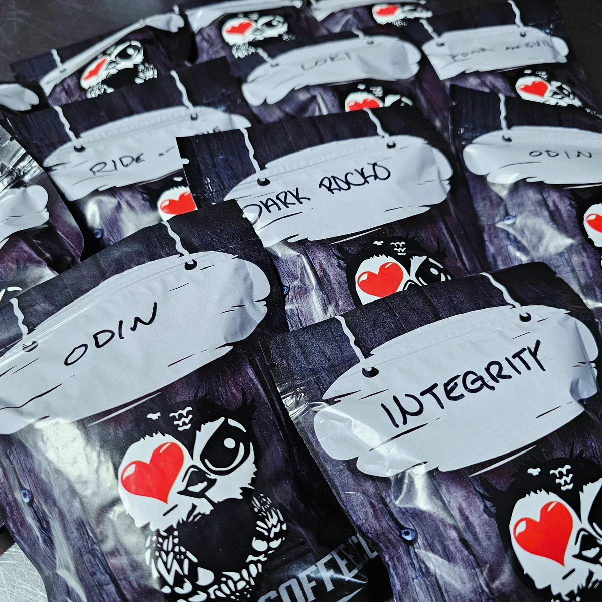 Iron Bean Coffee Company sampler bags with labels like Odin, Integrity, and Dark Rock featuring owl logo with heart eye