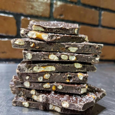 Stack of dark chocolate bark with pretzel pieces on a gray surface with brick wall background